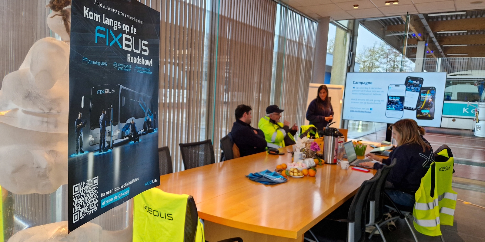 Vergaderzaal met kandidaten, met op de voorgrond de poster van de FixBus.